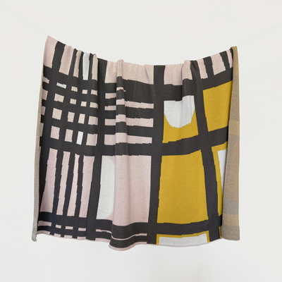 Modern Checkerboard Abstract Cotton Throw by Tuxberry & Whit, hanging on a line, featuring a unique pattern with mid-century modern vibes. The throw displays a stylish mix of light pink, mustard, charcoal grey, and light grey, made from 100% cotton, crafted in the USA