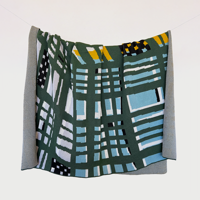 Eames-Inspired Tri-Plaid Cotton Throw hanging on a line, showcasing its unique corner convergence of plaid patterns in stillwater blue, white, black, hunter green, and mustard. Crafted from 100% cotton, this throw combines modern design with classic Eames inspirations, beautifully handcrafted in the USA