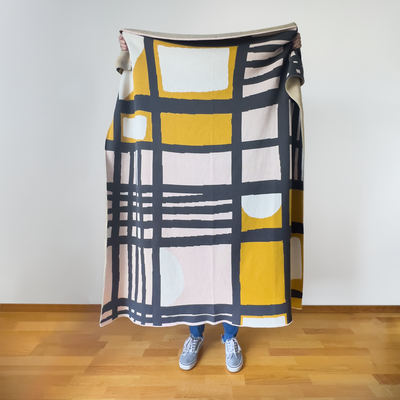 Person holding modern checker artist designed throw blanket displaying complete grid pattern with movement-creating shapes in muted colors