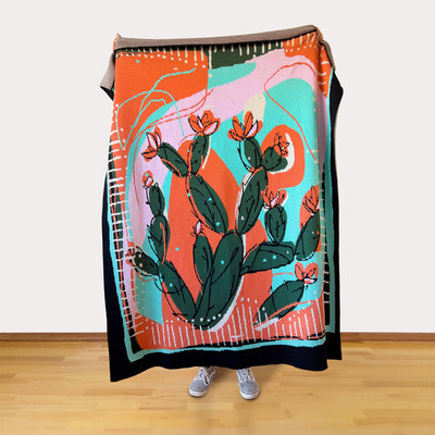 Person holding a colorful blanket with cactus design on a wooden floor.