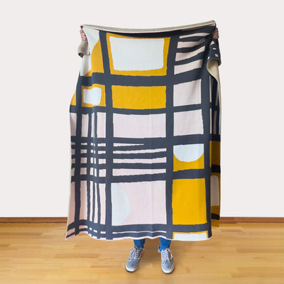 Person holding a colorful geometric-patterned blanket in a room with wooden flooring.