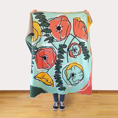 Person holding a colorful floral blanket against a white wall.