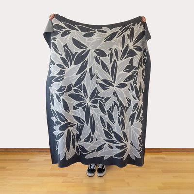 Person holding a large grays and white leaf floral patterned blanket against a plain background