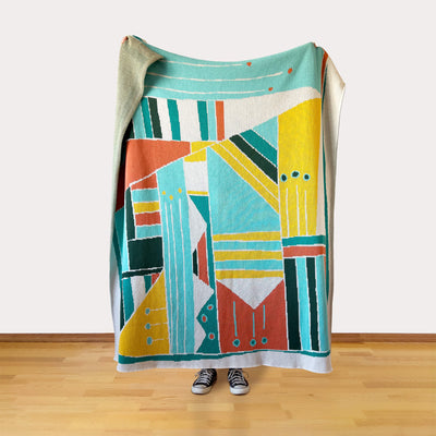 Colorful modern geometric-patterned blanket draped over a person on a wooden floor.