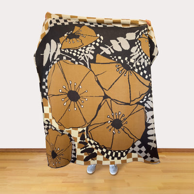 Floral patterned blanket in neutral colors draped over a person on a wooden floor with a white wall background