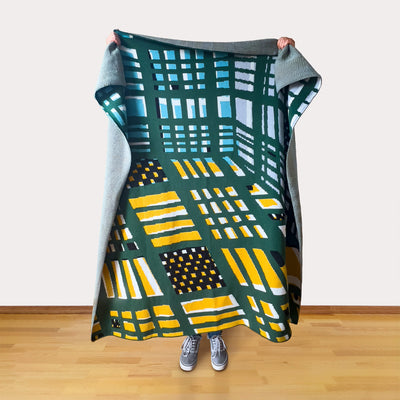 Person holding a colorful patterned blanket on a wooden floor.