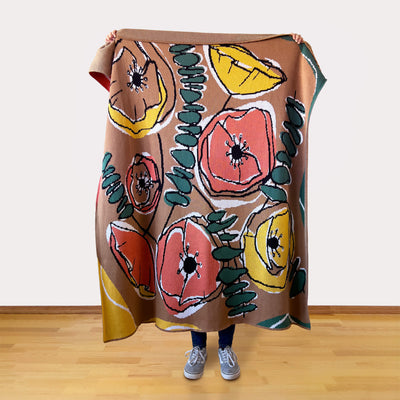 Person holding a colorful floral blanket  in retro browns, oranges, and yellows with a plain background.