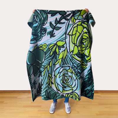 Person holding a floral patterned blanket with green and blue colors on a wooden floor.