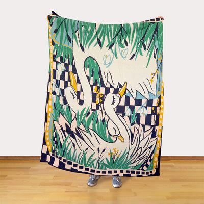 Person holding a colorful blanket with swan design on a wooden floor.