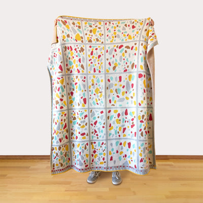 Colorful patterned blanket draped over a person on a wooden floor.