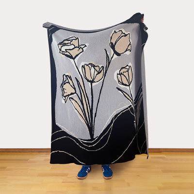 Person holding a black, white, gray, and tan colored blanket with tulip floral design on a wooden floor.