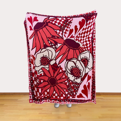 Decorative blanket with red and white floral and heart patterns on a wooden floor.