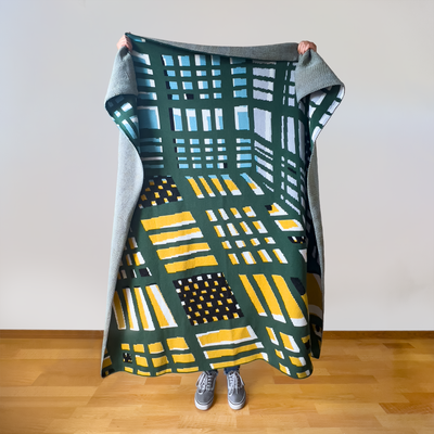 Architectural plaid artist designed throw blanket showing full perspective geometry pattern with converging grid lines in hunter green, blue, mustard yellow.