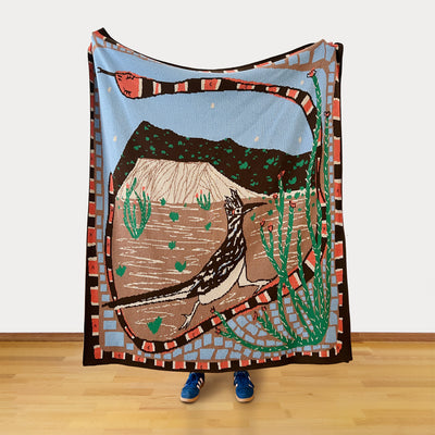 Person holding a colorful blanket with a desert scene design featuring a bird and cacti.