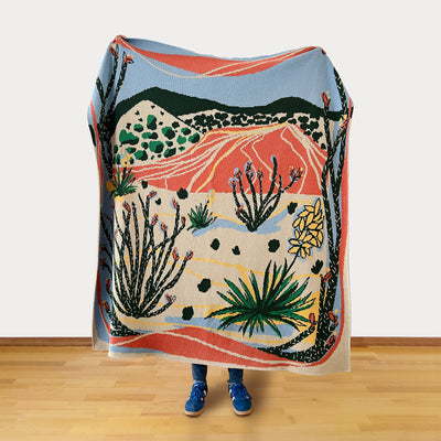Person holding a colorful desert-themed blanket with a person's legs visible at the bottom.