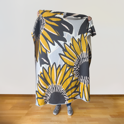Person holding modern sunflower artist designed throw blanket displaying full botanical pattern in subtle neutral color palette