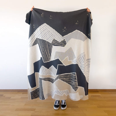 Person holding neutral knitted blanket depicting the mountains at night.