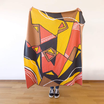 Person holding cotton knit blanket with colorful abstract designs and lines.