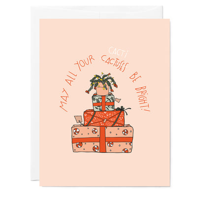 Hand illustrated greeting card featuring drawing of Christmas cactus on a pile of stacked presents. Hand lettered words read May All Your Cactuses (crossed out with Cacti) Be Bright. Red words, light pink background.
